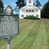 a historic white new england meeting house building sits on a smooth green lawn.