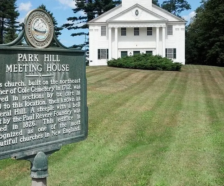 a historic white new england meeting house building sits on a smooth green lawn.