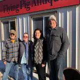 staff of flying pig antiques stand in front of their store wearing plaid and winter hats