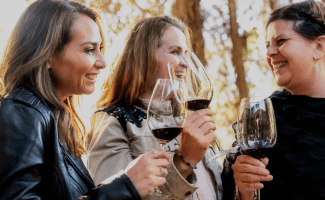 Three women enjoy tasting some red wine in the golden sunshine of an evening winery visit.