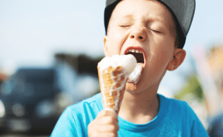 young boy in a baseball cap eats a very melty vanilla ice cream cone