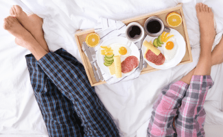 two people sit on a bed with a breakfast tray between them - you can only see their legs and feet!