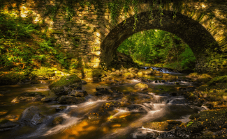 a stone arch bridge spans a rushing brook