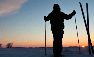 a person is silhouetted by the setting sun - their skiis are stuck standing up in the snow next to them.