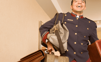 a bellhop carries too many bags, but he has a huge happy smile on his face