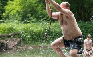 man hangs on rope and swings into the water - droplets are splashing up all around him