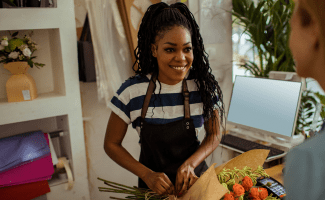 A woman ties up flowers for a customer. she smiles and wears an apron