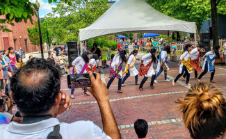 A crowd watches a troupe of dancers in an open brick square