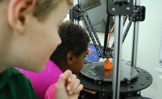 Two children watch a duck get printed on a 3-D printer