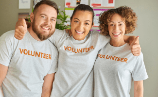 Three volunteers stand together with their arms around each others' shoulders.