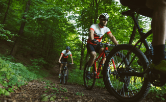 people in spandex biking team outfits ride on a flat trail through a green wooded area