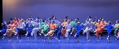 a stage full of kids dancing in different colored costumes under blue lighting