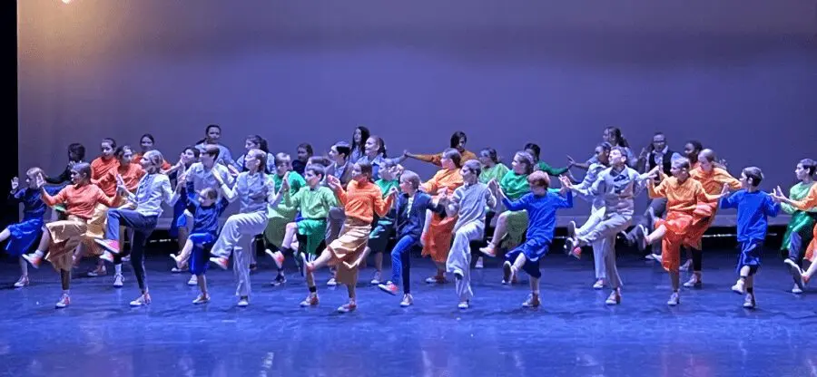 a stage full of kids dancing in different colored costumes under blue lighting