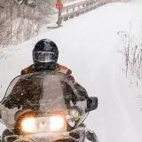 snowmobiler zooms over a bridge towards the camera