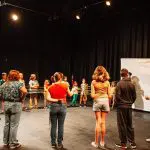 a circle of kids play a game in a blackbox theater