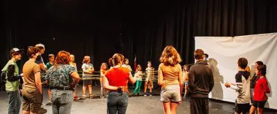 a circle of kids play a game in a blackbox theater