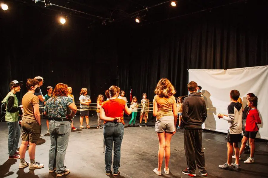 a circle of kids play a game in a blackbox theater
