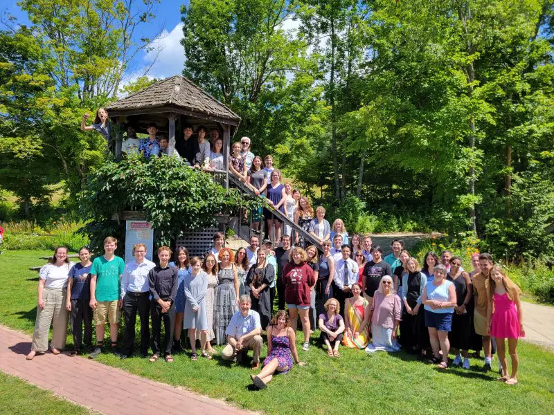 summer campers pose outdoors on and around a small building