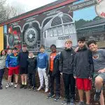 a group of middle schoolers smile in front of a mural of a train