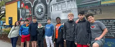 a group of middle schoolers smile in front of a mural of a train