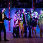 cabaret cast poses on stage in dark blue light