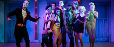cabaret cast poses on stage in dark blue light