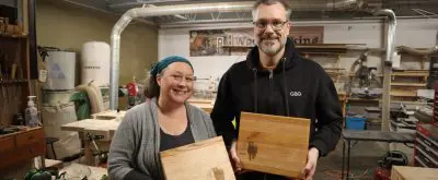 two people proudly pose with wooden cutting boards that they designed
