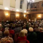 fully attended music concert in museum hall with wooden and white walls