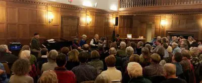 fully attended music concert in museum hall with wooden and white walls