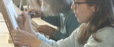 A group of artists works on easels in a classroom setting.