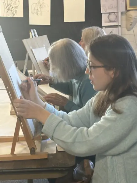A group of artists works on easels in a classroom setting.
