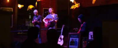 three musicians perform at the coffee house stage of Nova Arts, surrounded by art installation of glowing whales suspended from the ceiling