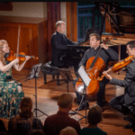 a string quartet performs, looking engagingly at one another