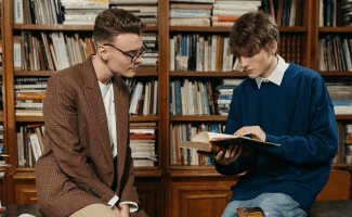 two young men look at a book in a library