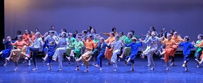 a stage full of kids dancing in different colored costumes under blue lighting