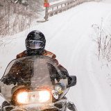 snowmobiler zooms over a bridge towards the camera