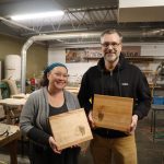 two people proudly pose with wooden cutting boards that they designed